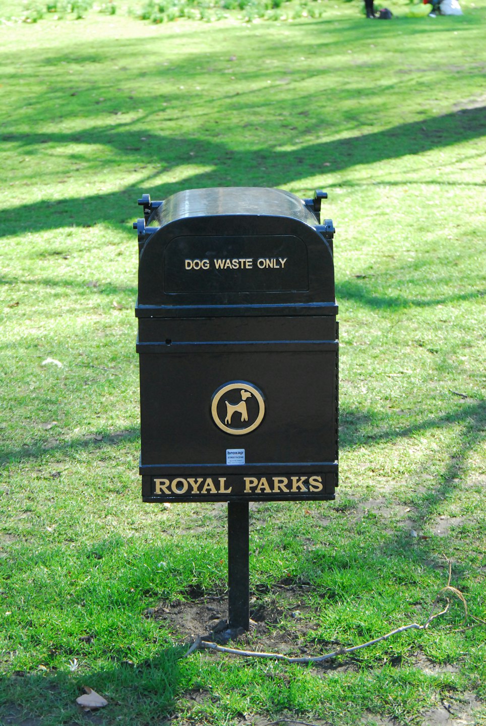 Dark dog waste bin with gold lettering on a grassy lawn.