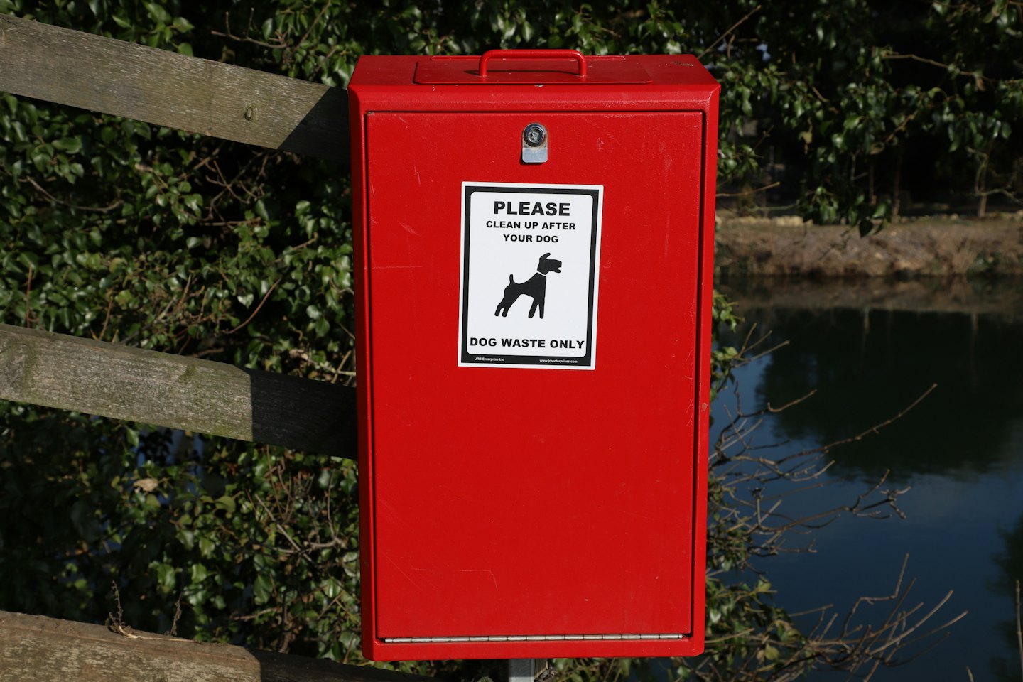 Red dog waste bin mounted on a wooden fence post.